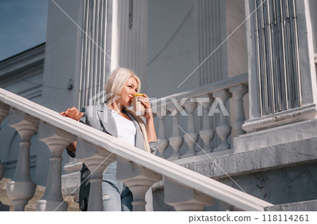 A woman is standing on a white staircase with a cup in her hand. She is smiling and looking up at the sky. 118114261