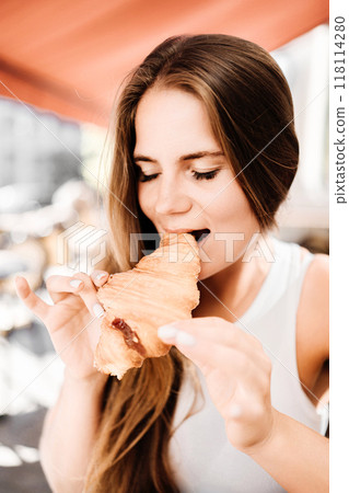 A woman is eating a croissant. The croissant is half eaten and has a jelly filling. 118114280