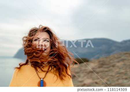 Portrait windswept hair happy woman against a backdrop of mountains and sea. Daylight illuminates the tranquil outdoor setting 118114309
