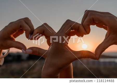 Hands Heart Sunset - Two hands forming a heart shape against the setting sun, symbolizing love and affection. 118114488