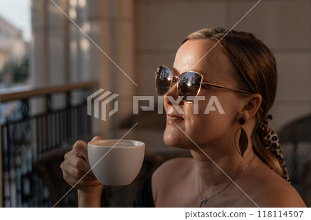 Woman Sunglasses Coffee - A woman in sunglasses sips coffee while looking out a window. Woman Sunglasses Coffee - A woman in sunglasses sips coffee while looking out a window. 118114507