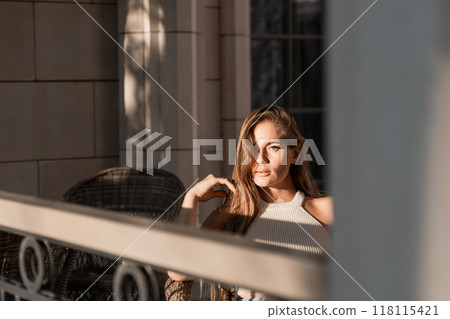 Woman Sunlight Balcony - A woman sits on a balcony in the sunlight. 118115421