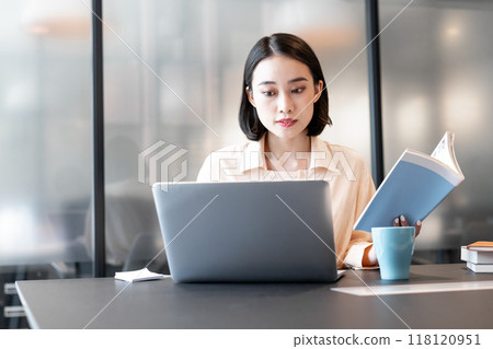 一位女士在電腦上工作，同時參考一本書 118120951