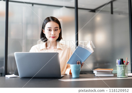 一位女士在電腦上工作，同時參考一本書 118120952