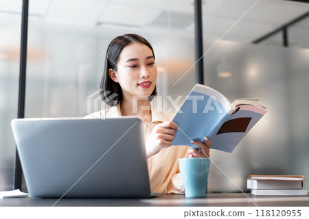 A woman working on a computer while referring to a book 118120955