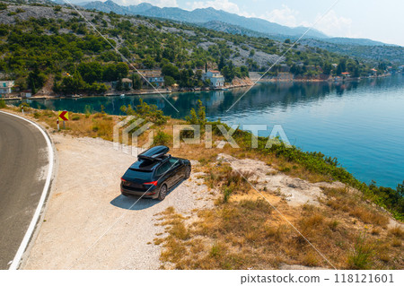 Car with roof box parked near road on cliff against azure sea. Suitable roadside spot for tourists to admire awesome seascape during trip to Croatia 118121601