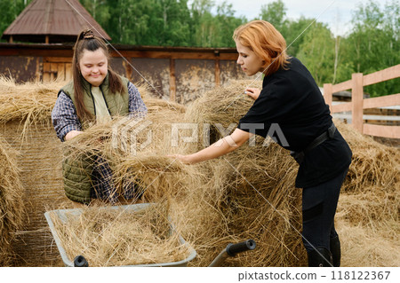 Two Women Gathering Hay Outdoors on Sunny Day 118122367