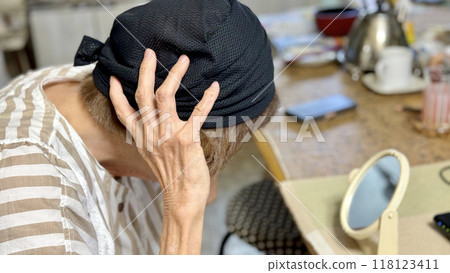 Elderly woman putting on a black hat while looking in the mirror Elderly woman putting on a black hat while looking in the mirror 118123411
