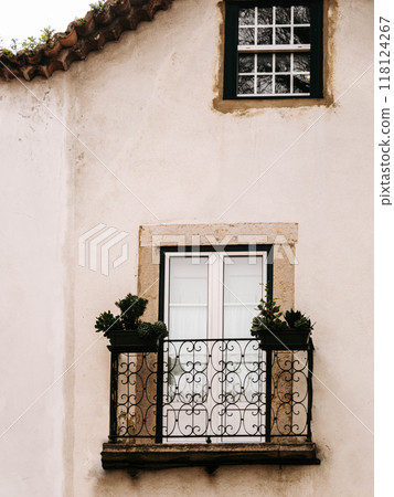 White wall of a residential building with a small balcony with decorative wrought iron and potted plants 118124267