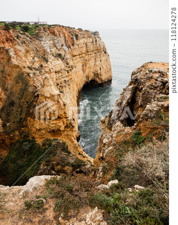 Rocky coastal cliffs with a natural arched shape, overlooking the clear blue water below 118124278