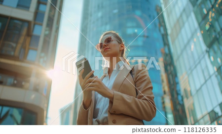 Confident businesswoman completing agreement on phone, standing in bustling city with skyscrapers Female executive making a successful deal 118126335