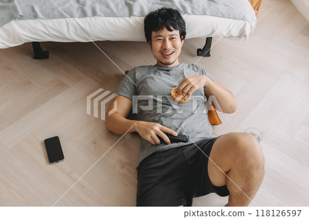 Man lying on the floor eating snack and laughing at the TV on weekends. 118126597
