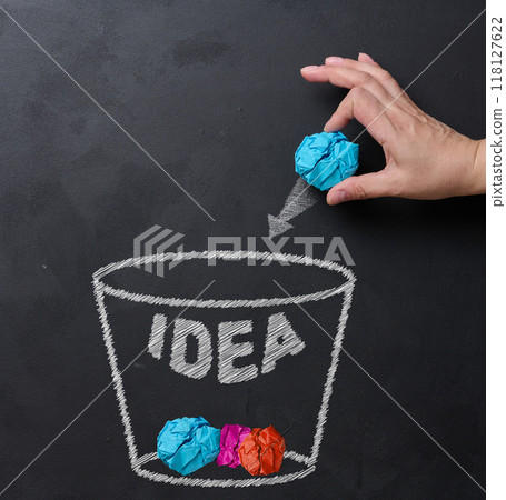 Process of idea rejection and creative improvement, hand throwing crumpled paper ball to basket with idea inscription. Paper balls inside a basket symbol of discarded 118127622