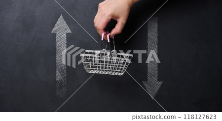 Concept of economic fluctuations and consumer behavior, featuring a hand holding a small shopping basket suspended between two arrows pointing up and down. Concept of economic fluctuations and consumer behavior, featuring a hand holding a small shopping basket suspended between two arrows pointing up and down. 118127623