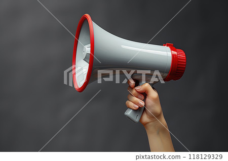 A close-up image of a person's hand holding a red and white megaphone against a dark background, symbolizing communication, announcement, and amplification 118129329