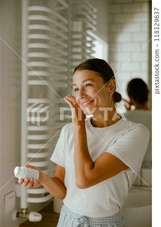 A woman is applying her skincare routine in a beautifully designed modern bathroom space 118129637
