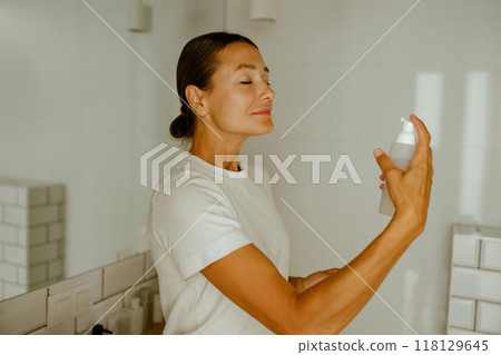 A woman in a beautifully bright bathroom is applying a skincare product with grace and care, 118129645