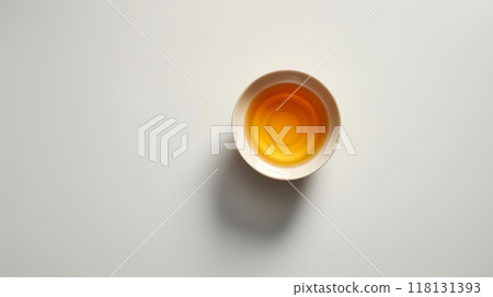 A small bowl sits alone on a white table, containing a golden liquid that reflects light 118131393