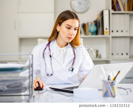 Focused woman doctor working in medical office using laptop 118132312