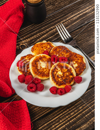 Cottage cheese pancakes with fresh raspberries on a white plate on the table Cottage cheese pancakes with fresh raspberries on a white plate on the table 118132990