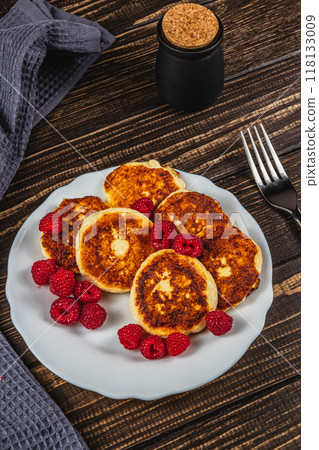 Cottage cheese pancakes with fresh raspberries on a white plate on the table Cottage cheese pancakes with fresh raspberries on a white plate on the table 118133009