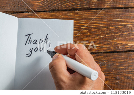 A person is writing a thank you note on a piece of paper on a wooden table 118133019
