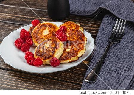 Cottage cheese pancakes with fresh raspberries on a white plate on the table Cottage cheese pancakes with fresh raspberries on a white plate on the table 118133023