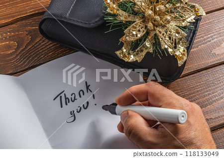 A man writes thank you on a piece of paper on a wooden table A man writes thank you on a piece of paper on a wooden table 118133049