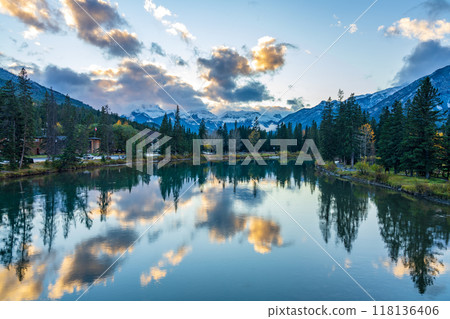 Bow River riverbank in autumn season sunset time. Beautiful fiery clouds reflect on water surface like a mirror. Beautiful nature scenery in Banff National Park, Canadian Rockies. 118136406