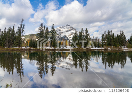 Banff National Park beautiful natural scenery. Cascade Mountain with blue sky, white clouds reflected on Bow River like a mirror in a snowy autumn sunny day. Town of Banff, Canadian Rockies. 118136408