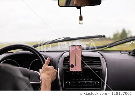 Rear view of a young traveler using a navigator on a mobile phone behind the wheel of a modern car . 118137005
