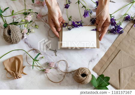 Marble desk with pink and blue flowers, postcard, kraft envelope, twine, cotton branch. Layout of Women's Day or Mother's Day, St. Valentine's Day, flat position, top view. 118137167
