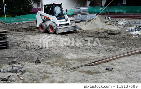 A small tractor works in the sand, filling up a hole. Shovels are on the ground. View from above. A small tractor works in the sand, filling up a hole. Shovels are on the ground. View from above. 118137599