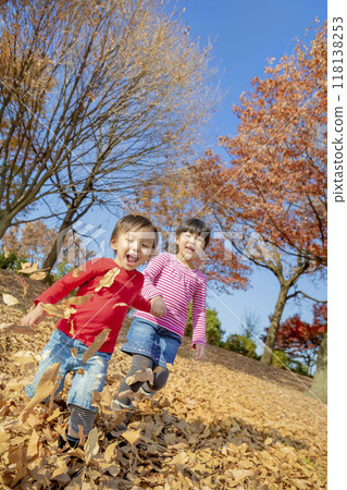 Older sister and younger brother playing in a park with autumn leaves 118138253