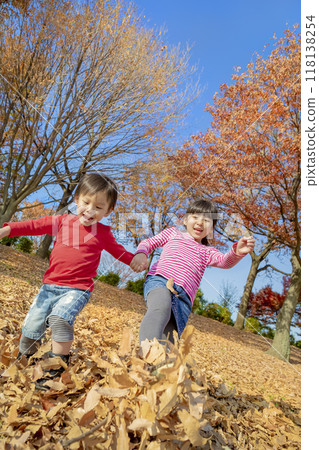 Older sister and younger brother playing in a park with autumn leaves 118138254