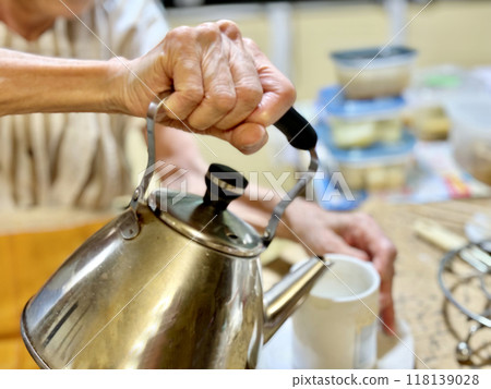 Elderly woman pouring tea in a kettle Elderly woman pouring tea in a kettle 118139028