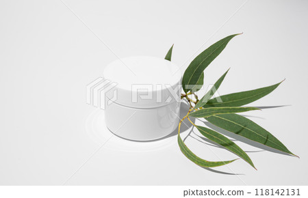 Face and body cream in a white jar on a light background with leaves and hard shadow. 118142131