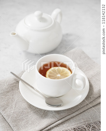 Tea with lemon in a white cup on a light background with  a teapot.  118142132