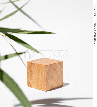 Empty wooden cube with shadows and green leaves on a white background. Empty wooden cube with shadows and green leaves on a white background. 118142145
