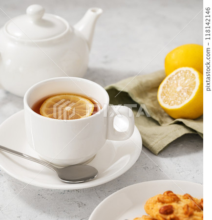 A cup of tea with lemon and homemade cookies on a light background with a white teapot and citrus A cup of tea with lemon and homemade cookies on a light background with a white teapot and citrus 118142146