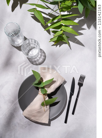Festive table setting with dark grey plate and glasses for a celebration with eucalyptus branches Festive table setting with dark grey plate and glasses for a celebration with eucalyptus branches 118142163