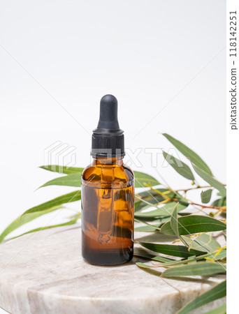 Face and body serum in bottle on a marble board on a white background with green leaves. 118142251