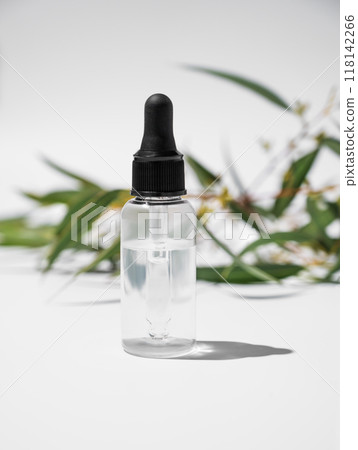Face and body serum in bottle on a white background with green leaves. 118142266