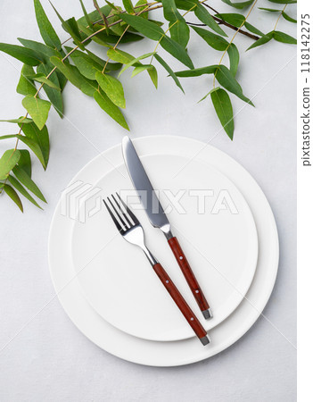 Festive table setting with white plates and cutlery on a light background with eucalyptus branches. 118142275