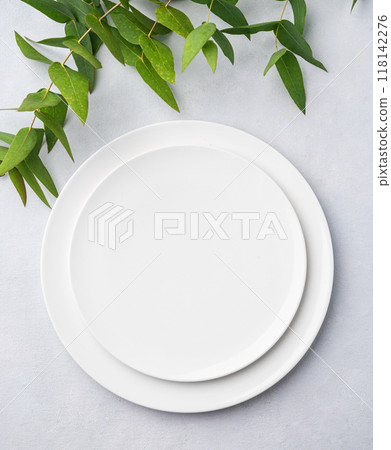 Festive table setting with white plates on a light background with eucalyptus branches. Festive table setting with white plates on a light background with eucalyptus branches. 118142276