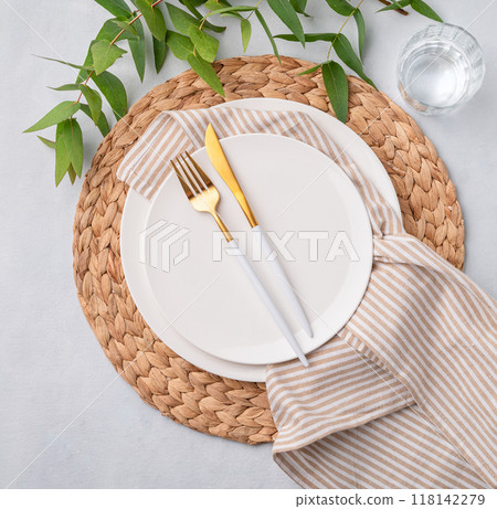 Festive table setting with white plates, glass and cutlery on a light background with napkin Festive table setting with white plates, glass and cutlery on a light background with napkin 118142279