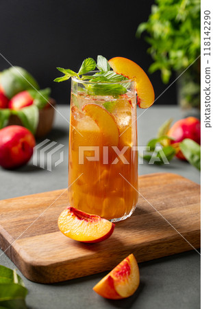 Peach tea with ice and mint on tall glass. Vegan homemade cold summer drink on a wooden board Peach tea with ice and mint on tall glass. Vegan homemade cold summer drink on a wooden board 118142290