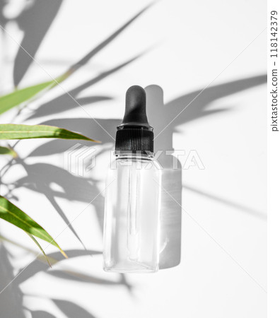 Body and face massage oil  on a white background with green leaves and shadow. 118142379