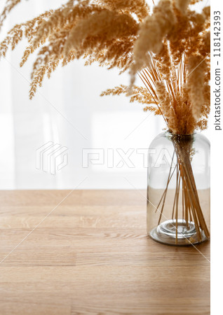 Stylish modern dry herb in a glass vase on a wooden background opposite a window 118142393
