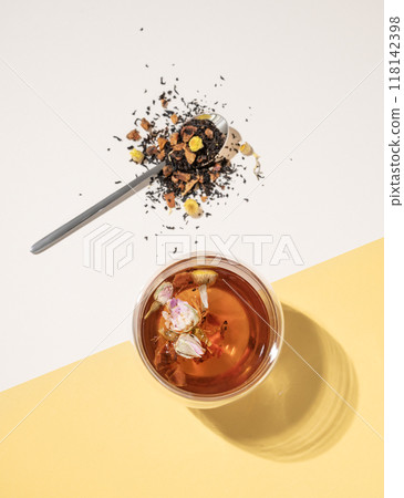 Creative flat lay of a glass cup of herbal tea with rose flowers on a yellow and white background  118142398
